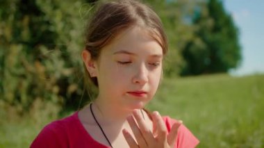 Sarı kivi yiyen, yumuşak meyveyi ısıran genç bir kız. Çocuk açık havada tatlı sarı kivinin tadını çıkarıyor, eşsiz lezzetin tadını çıkarıyor. Çocuk taze sarı kiviyi tadıyor, güneşli dokuyu takdir ediyor.