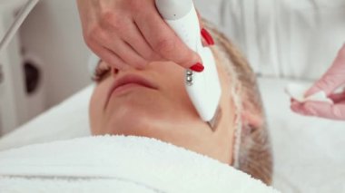 Güzellik kliniğinde deri spatulası tedavisi gören hasta kadın. Güzellik uzmanı yüz derisini yüzmek ve temizlemek için gelişmiş aletler kullanıyor. Profesyonel cilt bakım terapisi.