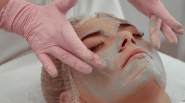 Kozmetik kliniğinde güzellik uzmanı tarafından uygulanan yaşlanma önleyici maske takan hasta. Güzellik uzmanı cilt bakımı için hastaya gençleştirici maske takıyor. Hasta sakince yatıyor.