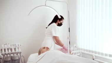 Kozmetik uzmanı kozmetoloji kliniğinde cilt bakımı sırasında aletleri hazırlıyor. Maske takan ve eldiven takan bir kadın uzman tedavi için gerekli malzemeleri düzenliyor. Bayan Güzellik Uzmanı hijyeni sağlıyordu.