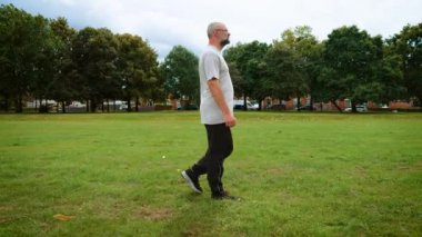 İngiltere 'de şehir parkında yürüyen bir adam. Yetişkin bir adam İngiltere 'deki yeşil alanda geziniyor. Orta yaş adamı İngiltere 'de eğlence alanında hareket ediyor. Büyük Britanya 'da halk parkında dolaşan bir adam.
