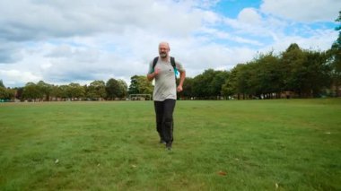 Adam İngiltere 'deki şehir parkında sırt çantasıyla yorgun koşuyor. Yetişkin bir adam İngiltere 'de yeşil alanda çanta taşımaktan yoruldu. Orta yaşlı bir adam eğlence alanında yorgunluk ve sırt çantasıyla koşuyor.