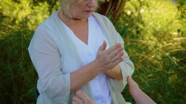 Masözün elleri bacağa masaj yapıyor, ayaklar erkeğe. Doğudaki ağaç altında kadın terapist tarafından gerçekleştirilen oryantal bacak masajı. Erkek ayağı ve ayağı için gençleştirici masaj. Rahatlama ayak masajı