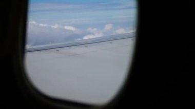 Uçak Pencereden Nefes Kesen Görüntü Hava Aracı Kanadı ve Serene Flight Over Clouds sırasında Mavi Gökyüzü. Kanatlar geniş mavi gökyüzünü kesiyor, alttaki tüylü beyaz bulutlarla.