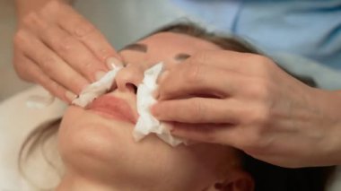 Güzellik prosedüründen önce müşteri yüzünü pamuk pedlerle silmek. Hazırlık için yüz derisini pamuk pedlerle temizliyorum. Tedavi için kadını nazikçe siliyor. Yumuşak pamuklu kadın yüzü hazırlanıyor.