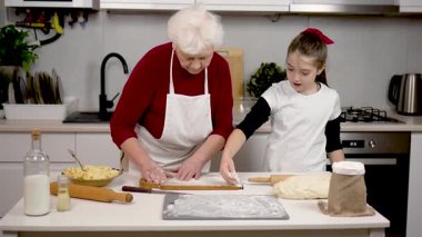 Büyükanne ve torun sıcak mutfakta hamur hazırlıyorlar. Üzerinde pişirme ürünleri olan beyaz un serpme tahtası. Evde tatil turtası pişirmenin tadını çıkar.