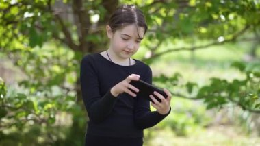 Mutlu kız parkta cep telefonuyla oyun oynuyor. Keyifli çocuk dışarıda eğlenen akıllı telefonlara hevesle bağlanır. Neşe ve konsantrasyon, mobil kablosuz teknolojiler, yenilikler