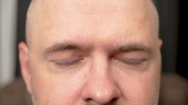 Ofiste uzun bir iş gününden sonra gözlerini kırpan bir adam. İş adamı gözlerini ovuşturuyor ve göz kırpıyor, zorlu bir iş gününden yorgun düşüyor. Erkek gözlerini kısar ve yorucu bir günün ardından yorgun gözlerle göz kırpar