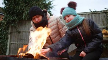 Soğuk bir günde kız ve erkek ateş yakıyor. Neşeli aile anları. Kış aktiviteleriyle vakit geçiriyoruz. Kız ve erkek kardeş soğuk havada ateşte ısınıyor.