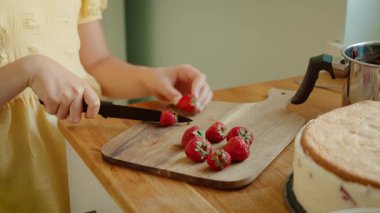 Tahta tahtada taze çilek dilimleyen kız. Çocuk pasta süslemesi için çilek hazırlıyor. Çocuk tatlı olarak kırmızı böğürtlen kesiyor.