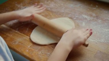 Elleriyle hamuru yuvarlayan kız pürüzsüz hamurun üzerinde yuvarlanan raptiye gibi. Yüzey, pürüzsüz hazırlanmak için un ile hafifçe tozlanmış. Hamur köftesi şekilleri için doku mükemmelleştiriliyor