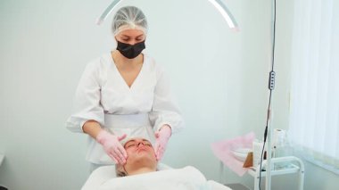 Güzellik uzmanı, yüz masajını lambanın altında yaparak gençleştiriyor. Cilt bakımında dinlenen bir kadın. Tedavi cilt sağlığını ve ışıltısını arttırır