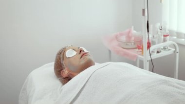 Kadın sakinleştirici cilt bakımı görüyor, rahatlatıcı atmosferden zevk alıyor. Dişi, cilt yenilenmesi için canlandırıcı yüz maskesi altında gevşemiş olarak yatıyor. Profesyonel bakım tanıtımının müşteri yardımları