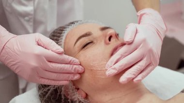 Gelişmiş estetik stüdyo uzmanı yüz tedavisi uyguluyor, hasta dinleniyor. Güzellik uzmanı cilde nazikçe masaj yapıyor, rahatlık sağlıyor. Cilt bakımı uzmanı rutini uyguluyor.