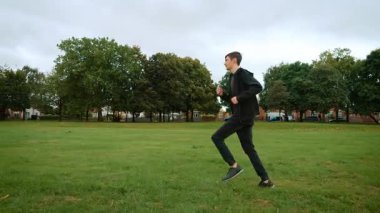 İngiltere 'deki şehir parkında yeşil çimlerde koşan bir genç. İngiltere 'deki şehir parkında çimenlik alanda koşan genç bir adam. İngiltere 'de halk bahçesinde çimlerin üzerinde koşan bir çocuk. Genç bir erkek.