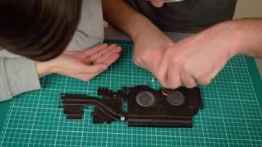 Baba oğluna dizüstü bilgisayar soğutma sistemini tamir etmeyi, tornavida tutmayı ve süreci açıklamayı öğretiyor. Erkek rehber çocuk ısıtıcıyı tamir ediyor, parçaları özenle birleştiriyor. Çocuğa daha havalı olduğunu gösteren adam.