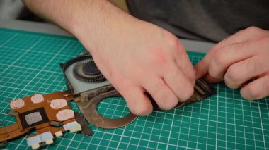 Baba ve oğul dizüstü bilgisayardaki toz ve çamuru temizleyip fan parçalarını dikkatlice tutuyorlar. Erkek rehber çocuk enkazı temizliyor, donanım temizliğini koruyor. Temizlikçi çocuk asistanı.