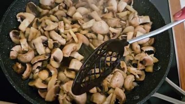 Modern Mutfak Ayarlarında Orta Sıcaklık Üzerine Karıştırma Aracı ile Tavada Taze Mantar Kızartma Akşam Yemeği Hazırlama. Tanınmayan kadın, şampiyonları tavada pratik spatulasıyla karıştırıyor.