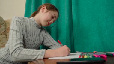 Kız kalemlerle çizim yaparken konsantre oluyor. Çocuk masada kağıt üzerinde resim yapıyor. Sanatsal aktivite sırasında kırmızı kalem kullanan bir çocuk. Renkli kalemlerin yakınındaki yaratıcı projeyle uğraşan kişi