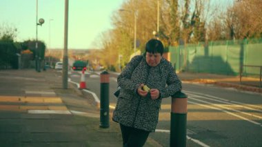 Kaldırımda duran ve yeşil elma yiyen bir kadın. Yaşlı kadın taze meyve yiyor. Kaldırımdaki yaşlı bayan sulu elmanın tadını çıkarıyor.