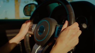 Aydınlık ve güneşli bir günde direksiyon sallayan tanınmayan eller. Parmaklar kırsal yol boyunca direksiyonu sorunsuzca tutuyor. Sürücü kontrol otomobili eğleniyor