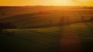 Gün batımı ışığı tarlalar boyunca uzanan uzun gölgeli tarlaların üzerine yayılıyor. Büyük Britanya 'da güneş batarken görkemli kırsal ve altın tarlalar. Ilık akşam parıltısı dalgalı otlakları aydınlatıyor.