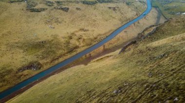 Araba otlak vadide asfalt yol boyunca gidiyor. Araç, İngiltere 'nin Peak District bölgesindeki manzaralı kırsalda ilerliyor. Mavi araba engebeli yollarda ilerliyor.