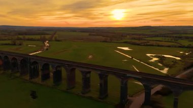 Zaman aşımına uğramış Brick demiryolu viyaoluğu altın gün batımının altında yeşil tarlaların üzerine uzanıyor. Hipersüratli Günbatımı eski İngiliz demiryolu viyaoluğunu nazikçe aydınlatıyor. Tarihi tren köprüsü uçsuz bucaksız