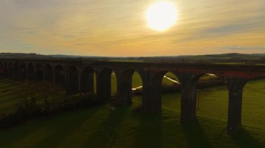 Güneşli vadide altından gökyüzü olan devasa demiryolu viyameti. Yeşilliklerle çevrili akşam ışığında muhteşem bir viyadük. Ilık altında kırsal alana yayılan ikonik tuğla köprü