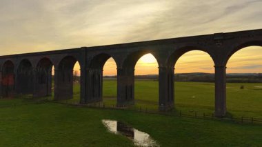 Yumuşak alacakaranlıkta yıkanmış İngiliz viyadük perspektifi. Gün batımında sakin vadide demiryolu viyadük manzarası