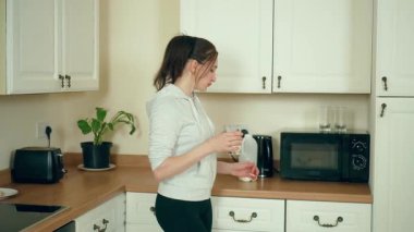 Modern beyaz mutfakta taze süt içen bir kadın. Çağdaş yemek alanında süt ürünü tüketen bir kadın. Şık mutfak alanında besleyici içeceklerden hoşlanan bir bayan.