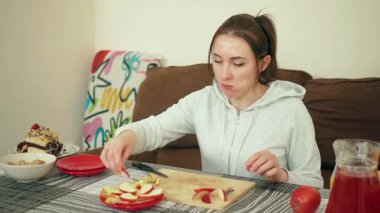 Sıcak yemek alanında, tabakta elma dilimleri düzenleyen bir kadın. Kadın, yeni kesilmiş meyveyi sıradan bir ev masasına yerleştiriyor. Rahat yaşam alanında sağlıklı bir şeyler hazırlayan bayan.