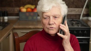 Evde, mutfakta cep telefonuyla konuşan, yüzünü çeviren, cep telefonuyla konuşan, telefon görüşmesinin keyfini çıkaran, kablosuz iletişimin tadını çıkaran son sınıf öğrencisi. Yüzünde kuru deri olan son sınıf öğrencisi bir kadın.