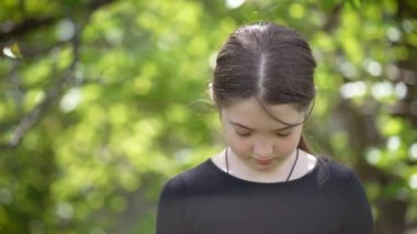 Genç Kız Yeşil Orman 'da Tek Başına Duruyor, Kafası Üzüntü içinde, Güneş Işığı Sessiz Öğleden Sonra Ağaçların Arasında Süzülüyor. Dışarıdaki küçük sevimli genç bayan, çocuk ifadesi. Doğadaki çocuklar