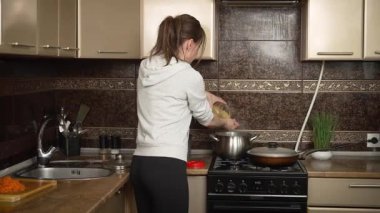 Genç bir kadın gaz sobasında makarna pişiriyor. Kadın mutfaktaki ocakta şehriye hazırlıyor. Mutfakta gaz ocağında makarna pişiren bir kadın.