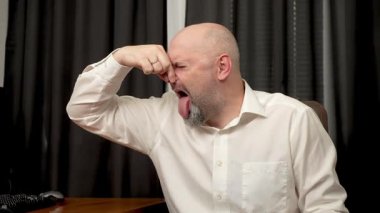 Burnunu elinle kapatan, buruşturan ve kötü kokudan geğiren bir adam. Burnunu eliyle tutan, yüzünü buruşturan ve pis koktuğu için geğiren bir adam. Burnunu çimdikleyen, ürkek ve iğrenç kokudan ağzı tıkanan bir adam.