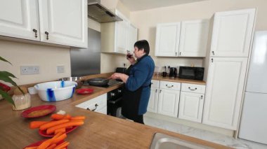 Mutfakta sebze pişiren bir kadın. İçki içerken tavada kadın karışımı karışımı. Bayan sobada ev yapımı yemek hazırlıyor. İçerde yemek yaparken birden fazla iş yapan kişi