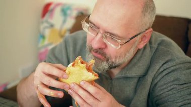 Yemek masasında peynir yiyen bir adam. Erkek, soslu ve soslu aromalı sandviçi seviyor. Adam yoğun bir şekilde ev yapımı aperatifin tadını çıkarıyor. Lezzetli ve dağınık yemekler yiyen bir insan.