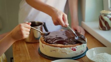 Oğlan ve kız çikolatalı pastayla pasta süslüyorlar. Genç bir oğlan ve genç bir kız tatlıya erimiş çikolata serpiyorlar. Kardeşler ev yapımı pastaya parlak çikolata kreması katıyor.