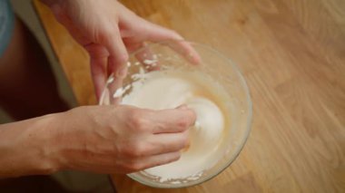Kadın tatlı hazırlamak için kaşık kullanarak cam kâseye krema karıştırıyor. Yemek yaparken yumuşak dokuya ulaşmak için kadın kremalı karışımı nazikçe katlıyor. Kırbaçlanmış kadın karışımı