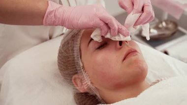 Kadın yüz temizleme sırasında yalan söylüyor, kozmetoloji kavramını vurguluyor. Hasta nazik cilt bakımı alıyor, güzellik prosedürlerine hazırlanıyor. Bireysel rahatlama