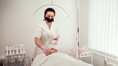 Kozmetik bilimci güzellik uzmanı kozmetoloji kliniğinde yaşlanma önleyici krem sürüyor. Kadın uzman, ürünleri nazikçe yüzlerine yayıyor. Hatta kapsama alanı sağlıyor. Güzellik uzmanı kadın tenine odaklanıyor