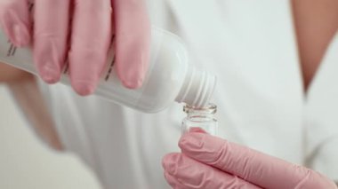 Pembe eldivenli estetisyen dikkatlice şişeye sıvı döküyor. Profesyonel klinikte kozmetik prosedürü için çözüm hazırlanıyor. Kesin tedavi uygulaması için cilt bakımı uzmanı