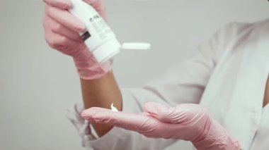 Cilt bakımı sırasında nemlendirici kremi eldivenli ellere döküyorum. Kozmetik tedavi için profesyonel hazırlık. Müşteri bakımı için hijyen ve hassasiyet sağlanması