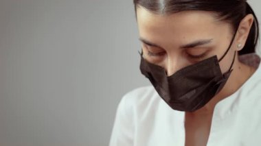 Siyah maskeli bir kadın güzellik uzmanı kozmetik dermatoloji kliniğinde çalışıyor. Kadın güzellik uzmanı kozmetik dermatoloji kliniğindeki prosedürlere dikkatle odaklanıyor. Bayan sakince görevlerini yerine getiriyor.