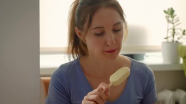 Dondurma yiyen bir kadın. Mavi tişörtlü kadın elinde tatlı tutuyor. Bayan içeride tatlı ikramlardan hoşlanıyor.