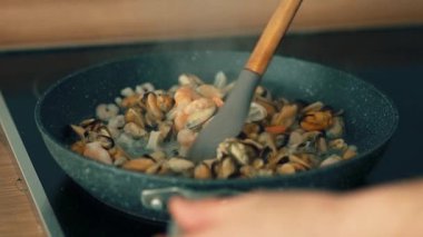 Kızartma tavasında karıştırılmış deniz ürünleri ve silikon spatula. Cızırdayan tavada karides, midye ve mürekkep balığı karışımı. Kabaran sosun içine çeşitli kabuklu deniz ürünleri atmak. Deniz mahsullerini karıştırmak için.