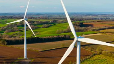 Manzaralı tarım arazileri üzerinde dönen yel değirmenleri yenilenebilir elektrik üretiyor. Açık gökyüzünün altında dönen rüzgar türbinleri ekolojik güç üretiyor. Türbin bıçakları renkli kırlarda dönüyor
