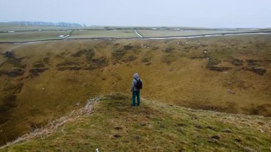 İnsan dağlarda uçuruma doğru adım atar, azim ve yücelik kavramı. İngiltere 'nin Peak District bölgesindeki engebeli arazide yürüyen bir yürüyüşçü. Sisli havada erkek kucaklaşması
