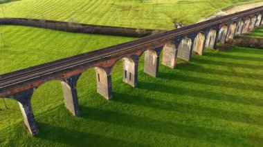 Hava manzaralı tarihi demiryolu viyadük yeşil alanlar üzerine uzun gölgeler bırakıyor. İngiliz demiryolu viyaolkü günbatımı renklerine gömüldü. Büyük tuğla köprü kırsal alanda sıcak altında uzanır.